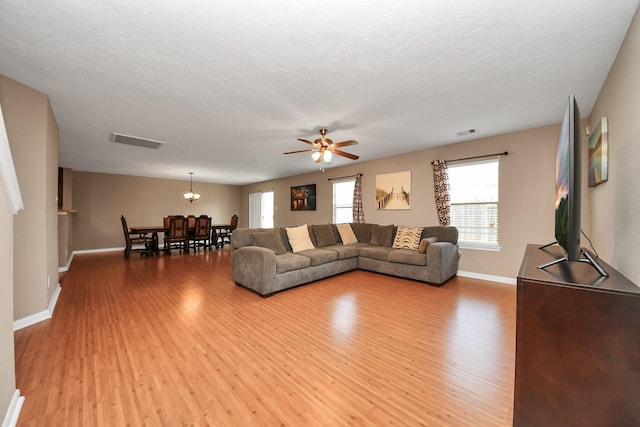 living room with ceiling fan, a textured ceiling, and light wood-type flooring