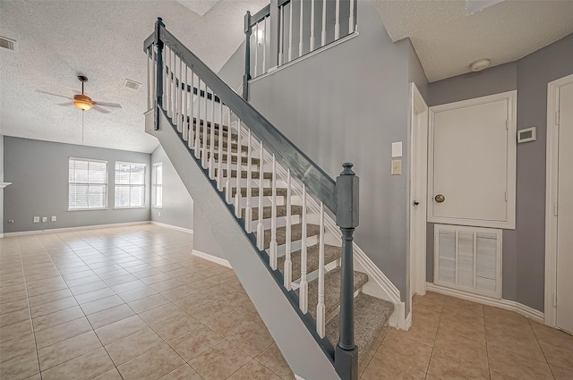 staircase with vaulted ceiling, ceiling fan, tile patterned flooring, and a textured ceiling