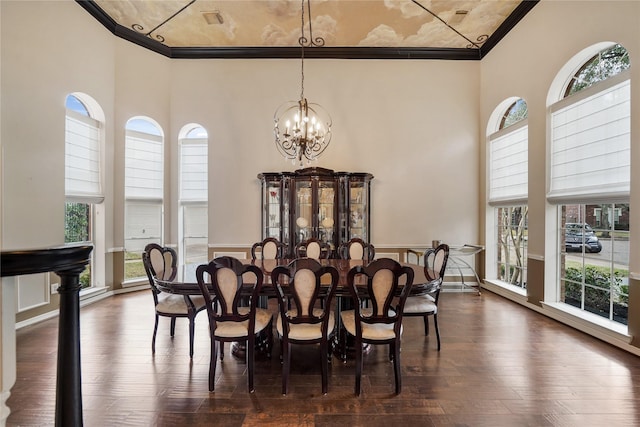 dining room with dark wood-type flooring, an inviting chandelier, ornamental molding, plenty of natural light, and a towering ceiling