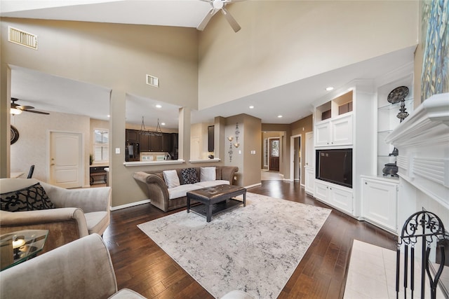 living room featuring dark hardwood / wood-style floors, ceiling fan, and a towering ceiling