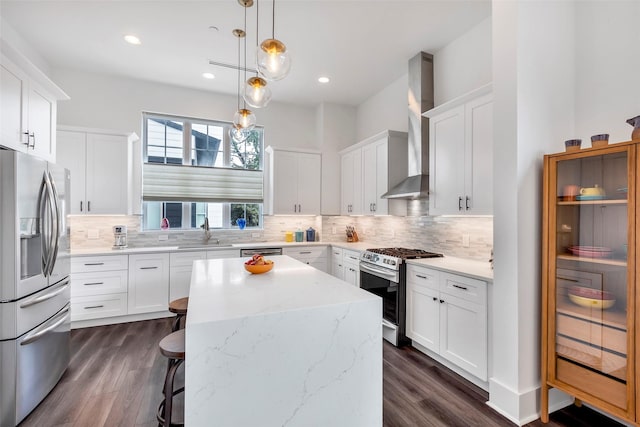 kitchen with sink, appliances with stainless steel finishes, a kitchen island, wall chimney range hood, and white cabinets