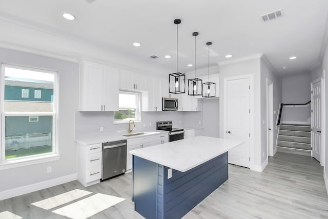 kitchen with a kitchen island, decorative light fixtures, white cabinetry, sink, and stainless steel appliances