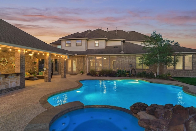 pool at dusk with an in ground hot tub and a patio