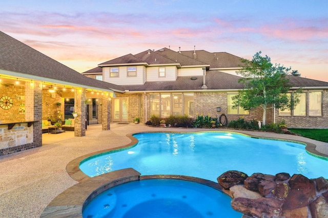 pool at dusk featuring a patio and an in ground hot tub