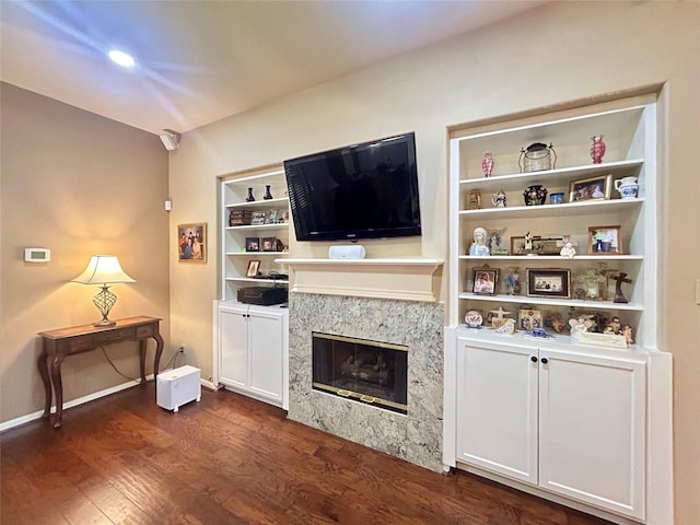 living room featuring dark wood-type flooring, a fireplace, built in shelves, and baseboards