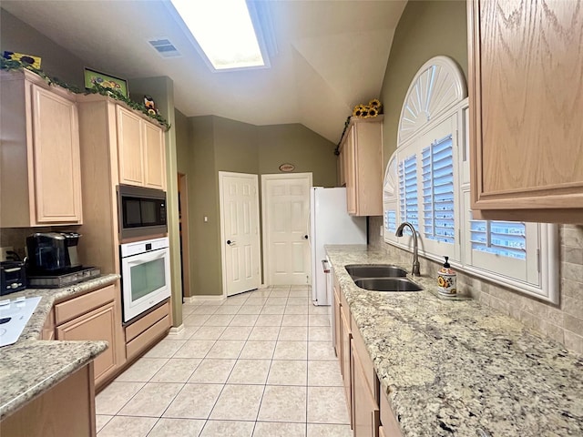 kitchen with white appliances, a sink, visible vents, light brown cabinetry, and lofted ceiling with skylight