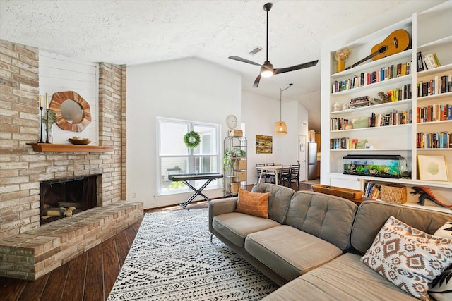 living room featuring vaulted ceiling, a textured ceiling, built in features, hardwood / wood-style flooring, and a fireplace