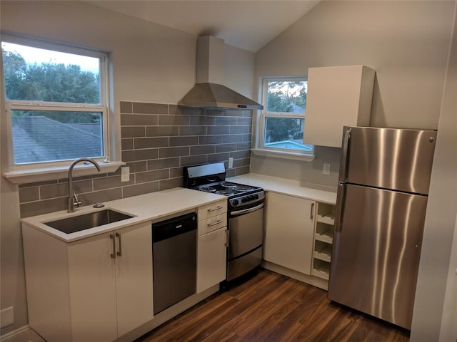 kitchen with wall chimney range hood, sink, stainless steel appliances, tasteful backsplash, and white cabinets