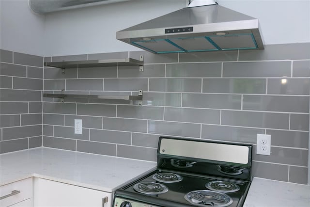 kitchen with tasteful backsplash, white cabinetry, exhaust hood, light stone countertops, and stainless steel electric range