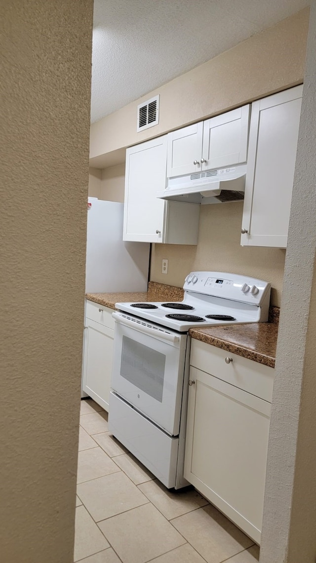 kitchen featuring white electric range oven, light tile patterned floors, a textured ceiling, and white cabinets