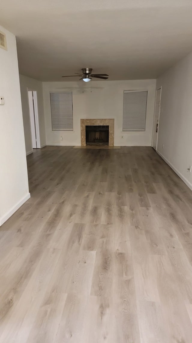 unfurnished living room with light hardwood / wood-style flooring, a premium fireplace, and ceiling fan