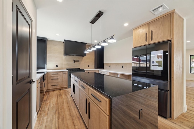 kitchen with a center island, decorative backsplash, decorative light fixtures, dark stone counters, and light wood-type flooring