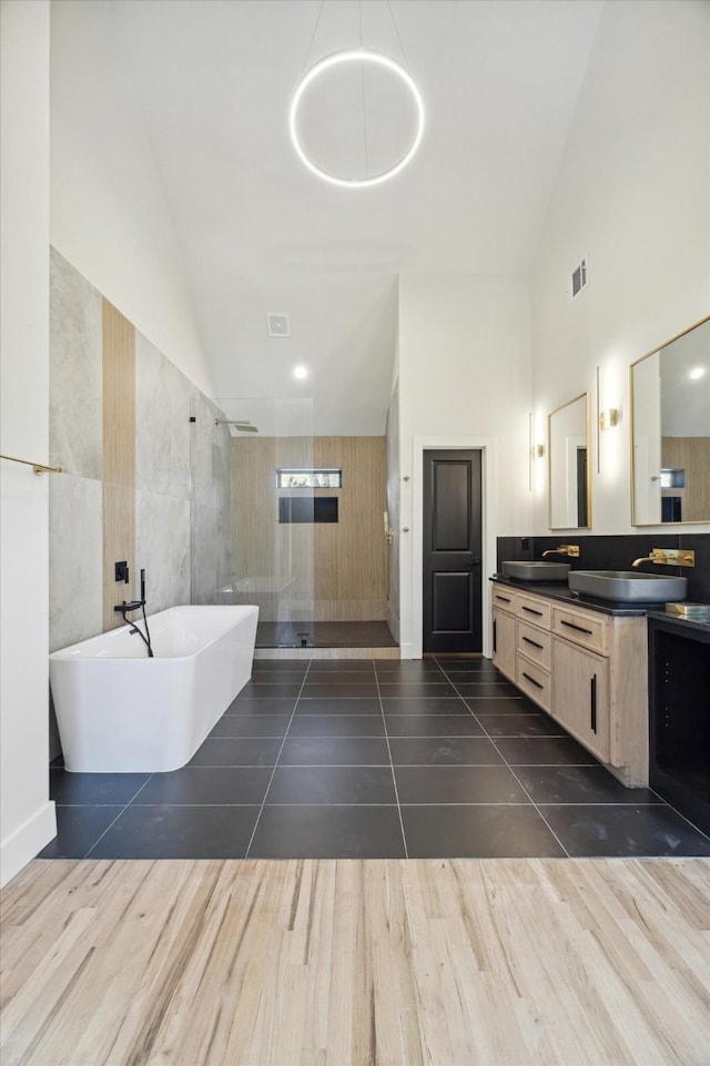 bathroom with hardwood / wood-style floors, high vaulted ceiling, independent shower and bath, tile walls, and vanity