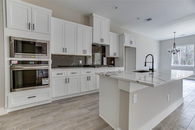 kitchen featuring stainless steel appliances, a center island with sink, white cabinets, and light stone counters