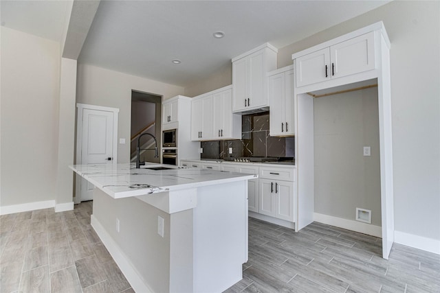 kitchen with white cabinetry, light stone countertops, a kitchen island with sink, and sink