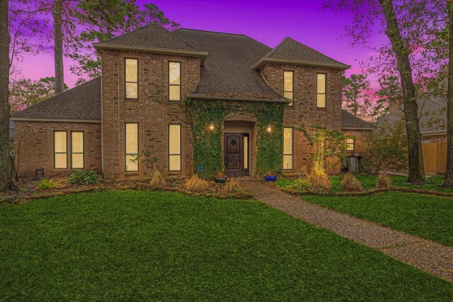 view of front of house featuring brick siding, a front yard, cooling unit, and a shingled roof