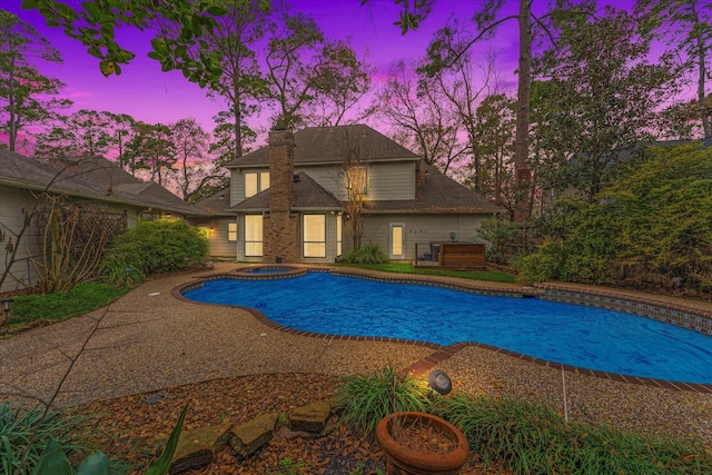 pool at dusk featuring an in ground hot tub and a patio area