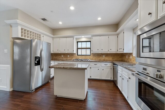 kitchen featuring a kitchen island, appliances with stainless steel finishes, tasteful backsplash, white cabinets, and light stone counters