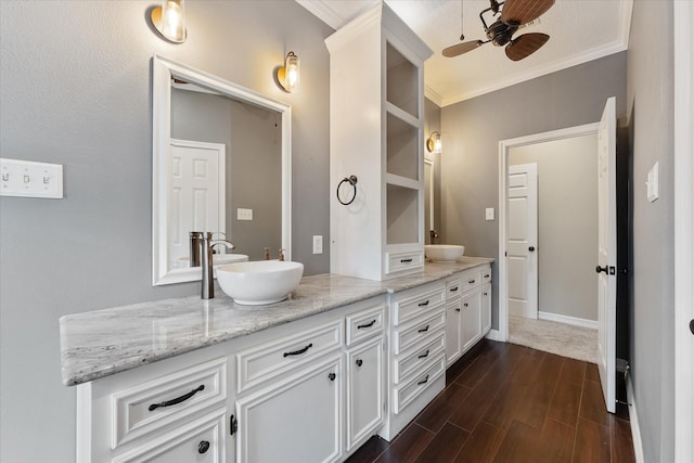 bathroom featuring wood finish floors, double vanity, ornamental molding, a ceiling fan, and a sink