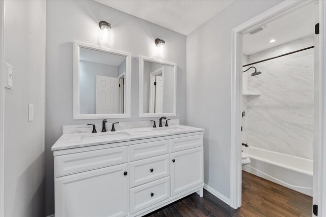 full bathroom with hardwood / wood-style flooring, vanity, tiled shower / bath combo, and toilet