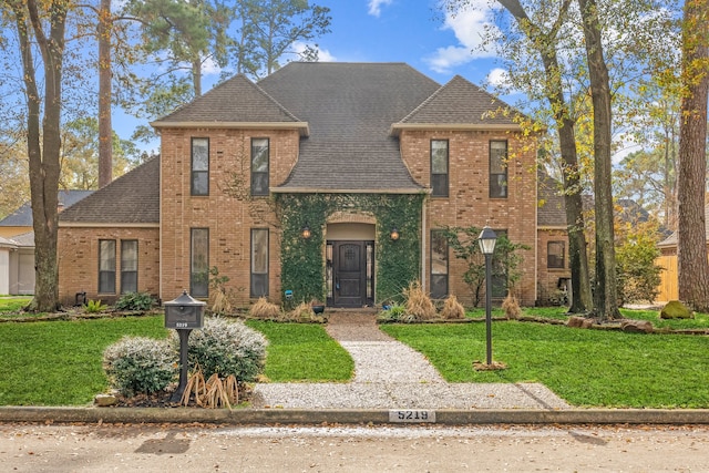 view of front of home with a shingled roof, a front yard, and brick siding