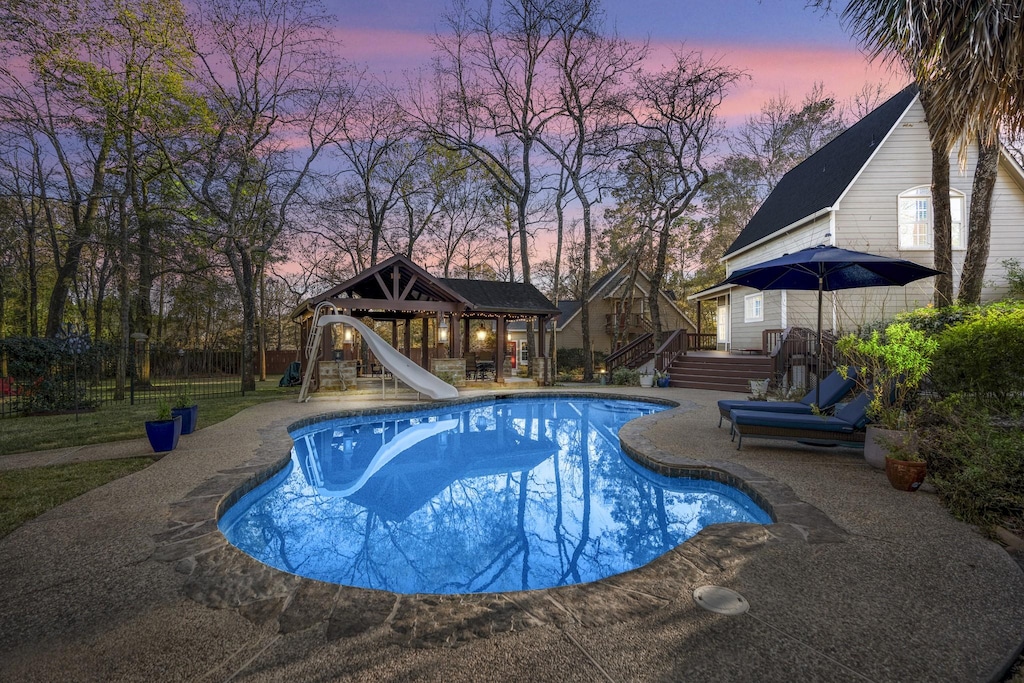 pool at dusk featuring a gazebo and a water slide