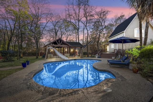 pool at dusk featuring a gazebo and a water slide