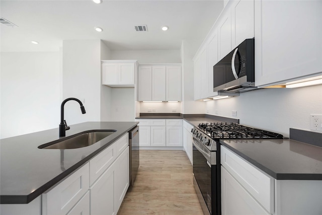 kitchen featuring appliances with stainless steel finishes, an island with sink, sink, white cabinets, and light hardwood / wood-style flooring