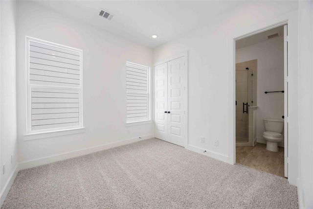 unfurnished bedroom with a closet, ensuite bath, and light carpet