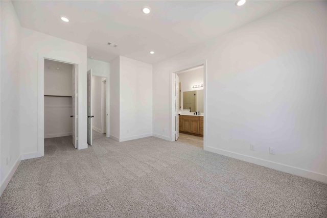 unfurnished bedroom with light colored carpet, ensuite bath, and a walk in closet