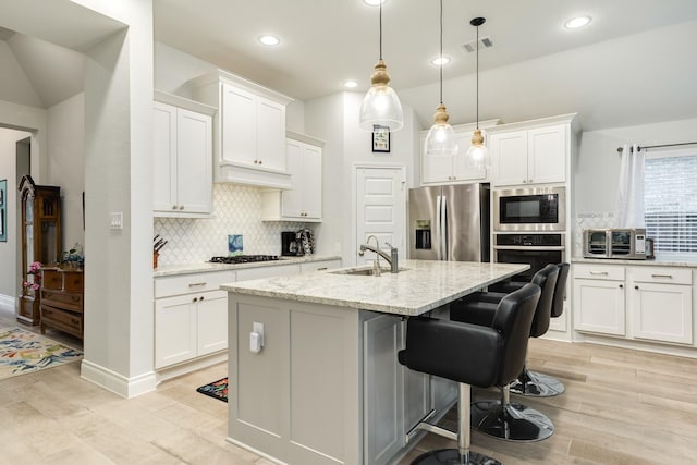 kitchen with stainless steel fridge, light stone countertops, a center island with sink, and white cabinets