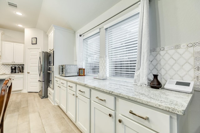 kitchen featuring tasteful backsplash, light stone countertops, and white cabinets