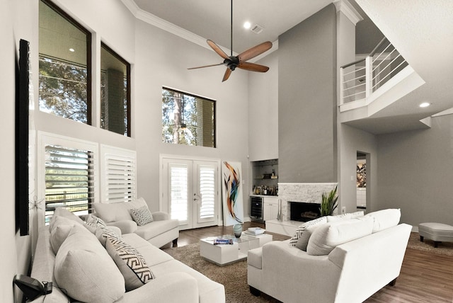 living room featuring crown molding, a towering ceiling, dark hardwood / wood-style floors, a fireplace, and french doors