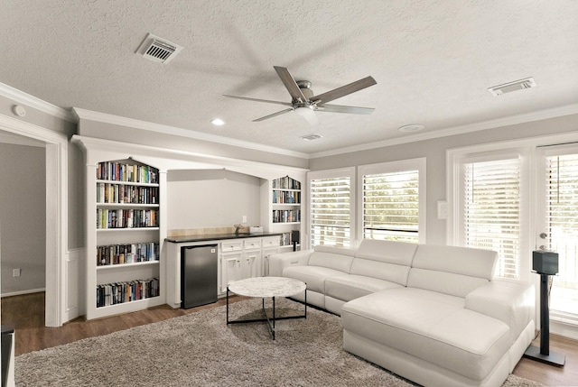 living room with ceiling fan, ornamental molding, a textured ceiling, and light wood-type flooring