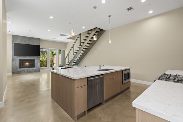 kitchen with sink, a large island with sink, a large fireplace, appliances with stainless steel finishes, and pendant lighting