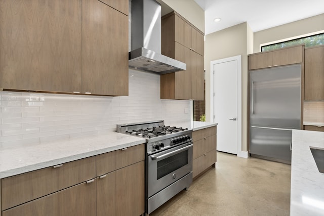 kitchen featuring wall chimney range hood, backsplash, light stone countertops, and high quality appliances