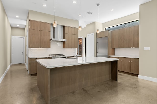 kitchen with decorative light fixtures, an island with sink, sink, built in refrigerator, and wall chimney range hood