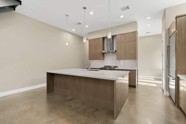 kitchen with wall chimney exhaust hood, light stone counters, decorative light fixtures, an island with sink, and decorative backsplash