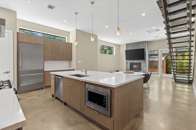 kitchen with sink, built in appliances, pendant lighting, a fireplace, and a kitchen island with sink