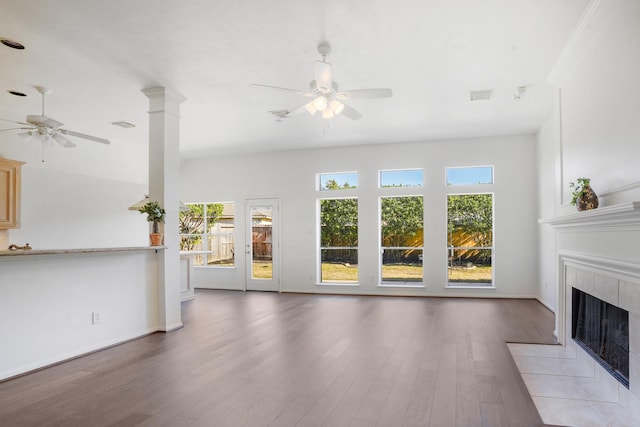 unfurnished living room featuring ceiling fan, wood-type flooring, and a tiled fireplace