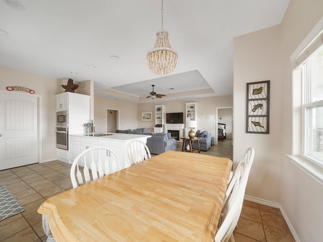 tiled dining space with a raised ceiling, sink, and ceiling fan with notable chandelier