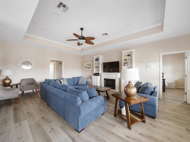 living room featuring crown molding, light wood-type flooring, and a tray ceiling