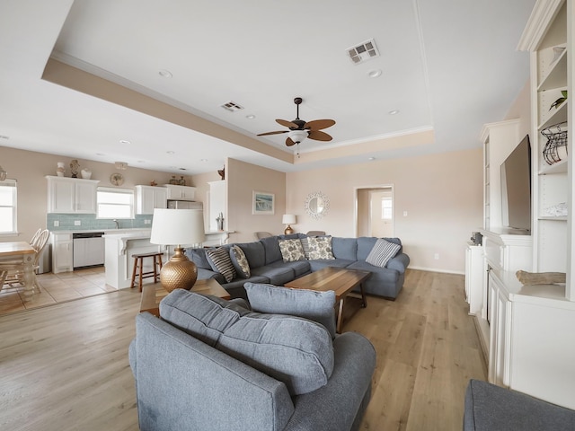 living room featuring crown molding, a tray ceiling, ceiling fan, and light wood-type flooring