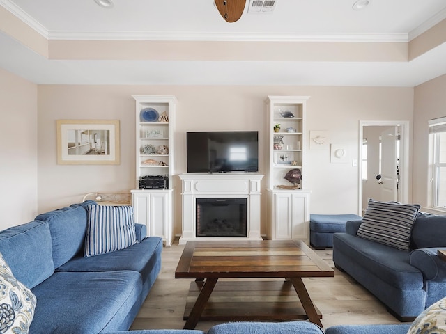 living room featuring crown molding, a raised ceiling, and light wood-type flooring