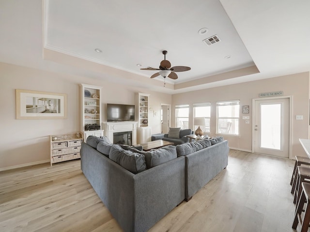 living room with a raised ceiling, ceiling fan, crown molding, and light wood-type flooring