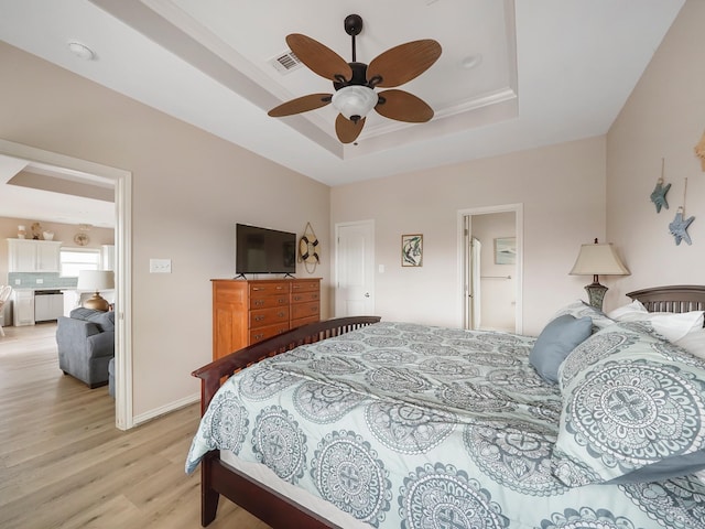 bedroom with ceiling fan, a tray ceiling, and light hardwood / wood-style floors