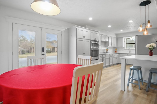 dining space with sink, french doors, a textured ceiling, and light wood-type flooring