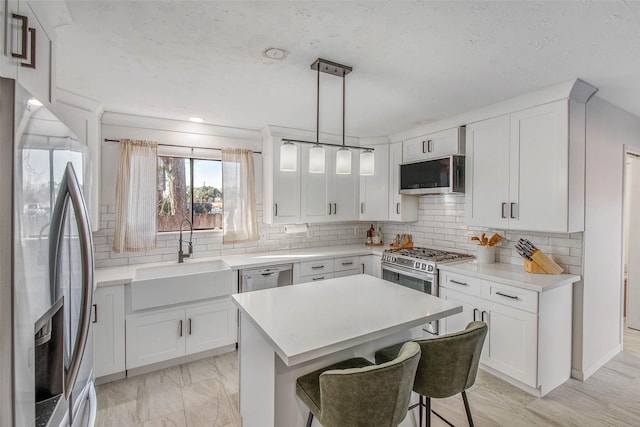 kitchen featuring sink, decorative light fixtures, appliances with stainless steel finishes, a kitchen island, and white cabinets