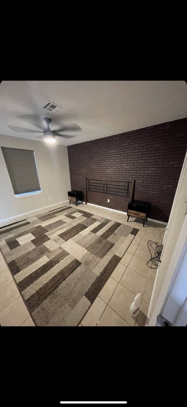 interior space featuring light tile patterned flooring, ceiling fan, and brick wall