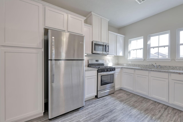 kitchen featuring white cabinetry, stainless steel appliances, light stone countertops, and light hardwood / wood-style flooring